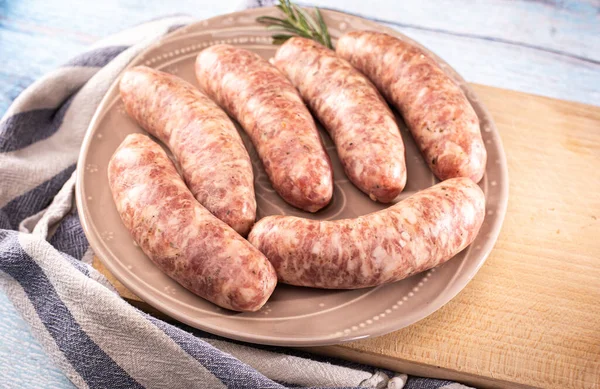 Traditional steamed white sausage on a plate, on a cutting board, on a wooden background. Rustic composition with white boiled sausage and fresh rosemary. Easter delicacy.