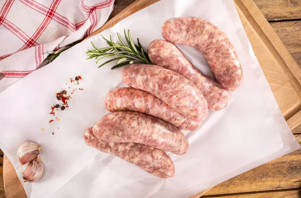 Rustic composition with white sausages, spices and fresh rosemary. Easter delicacy. Traditional Polish raw white sausage on a white paper, on a wooden background.