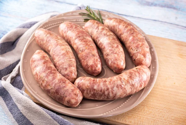 Traditional steamed white sausage on a plate, on a cutting board, on a wooden background. Rustic composition with Polish white boiled sausage and fresh rosemary. Easter delicacy.