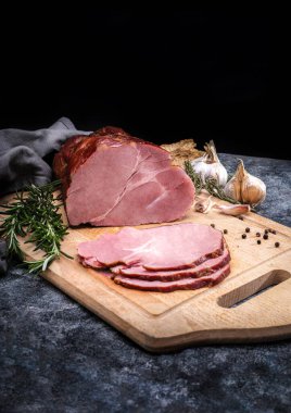 Smoked ham sliced on a wooden cutting board. Composition with Polish pork meat cold cuts, meat products, herbs, garlic and spices, vertical photo. 