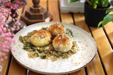Potato dumplings, Polish knedle with strawberries served on a young cabbage with dill and breadcrumbs. Dumpling filled with fruit on a modern plate, on a wooden table, selective focus.