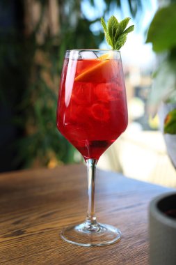 Kırmızı kokteyl, spritz, uzun bardakta bir içki, buz küpleri, portakal dilimleri ve nane yaprakları, siyah taş arka planda, seçici bir odak noktası..