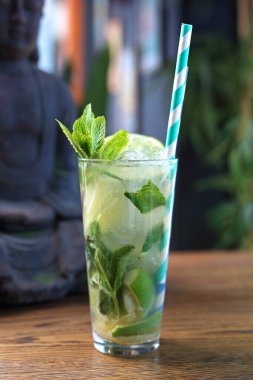 Mojito iç. Küba kokteyli, rom, nane şekeri, esmer baston şekeri, kireç ve ezilmiş buzdan yapılmış uzun bir bardakta, ahşap bir masada. Alkolik içki, seçici odaklanma. Kağıt kamışlı saf mojito..