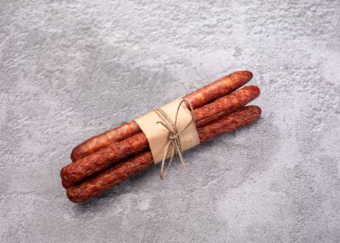 Polonya usulü kabanosi sosisi. İnce kuru sosis, eko gıda kağıdıyla sarılmış ve iple bağlanmış gri mermer arka planda. Tütsülenmiş et, et ürünü, üst manzara..