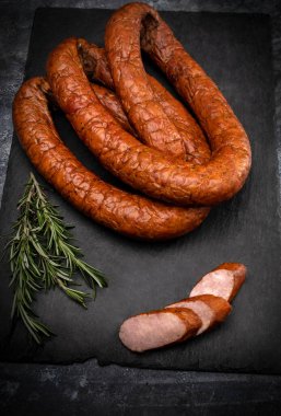 Siyah taşlı arka planda tütsülenmiş, halka şeklinde sosis. Geleneksel Polonya et soslu ve taze otlu kompozisyon.