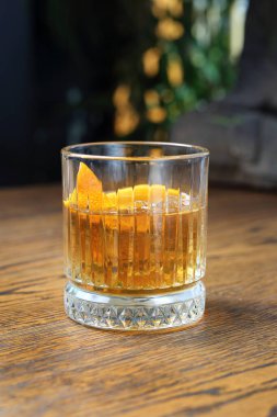 Eski moda burbon kokteyli. Klasik viski, şekerli viski, acı angostura ve portakal aromalı garnitür, eski moda bir bardakta, ahşap bir masada..