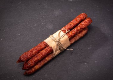 Polonya usulü kabanosi sosisi. İnce kuru sosisler, eko gıda kağıdıyla sarılmış ve iple bağlanmış, siyah taş zemin üzerinde, tahtada, karatahtada. Tütsülenmiş et, et ürünü, üst manzara..