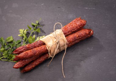 Polonya usulü kabanosi sosisi. İnce kuru sosisler, eko gıda kağıdıyla sarılmış ve iple bağlanmış siyah taş zemin üzerinde, maydanozla süslenmiş bir karatahtaya. Tütsülenmiş et, et ürünü..