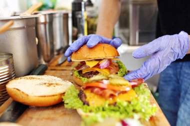 Hamburger yapıyorum. Bir hamburgeri koruyucu eldivenlerle hazırlamak, bir yemek kamyonunda, bir fast food restoranında, bir sokak yemeği pazarında, yakın plan, seçici odaklanma.