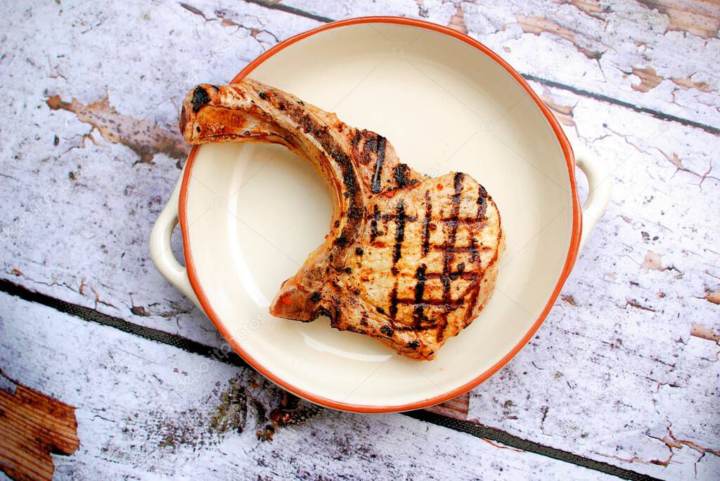 Grilled lamb chop, steak with bone, on a white plate, on a wooden rustic background, top view. Culinary concept.