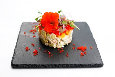 Karides salatası, yakın plan. Doğranmış karides, avokado, portakal ve tobiko soslu karides, yenilebilir çiçekle süslenmiş, siyah taştan bir tabakta, beyaz arka planda izole edilmiş..