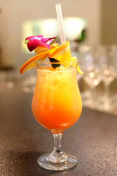 Tequila sunrise cocktail in a glass, on a stone counter. A drink with layered colors, made of orange juice, grenadine, tequila, decorated with orange zest and flower.