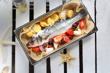 Sebzelerle dolu bir levrek, fırın kabına baharat serpiştirilmiş, beyaz bir masada. Parşömen kağıdıyla kaplanmış bir tavada balık pişirmek.. 