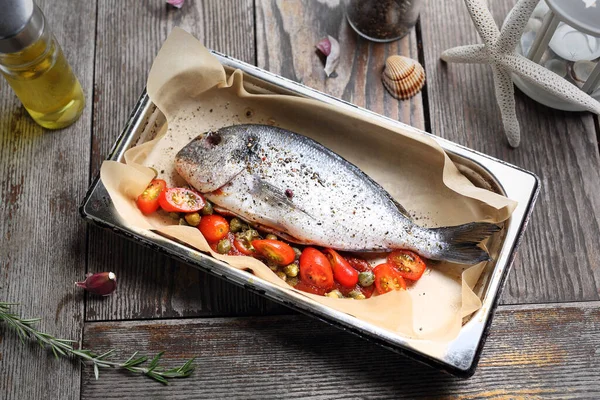 Tüm deniz çipurası sebzelerle dolu, ahşap bir masada, fırın kabına baharat serpiştirilmiş. Parşömen kağıdıyla kaplanmış bir tavada balık pişirmek.. 