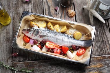 Sebzelerle dolu bir levrek, fırın kabına baharat serpiştirilmiş, beyaz bir masada. Parşömen kağıdıyla kaplanmış bir tavada balık pişirmek.. 
