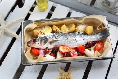 Sebzelerle dolu bir levrek, fırın kabına baharat serpiştirilmiş, beyaz bir masada. Parşömen kağıdıyla kaplanmış bir tavada balık pişirmek.. 