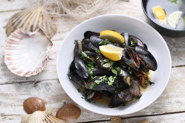 Mussels in wine-butter sauce, sprinkled with freshly chopped parsley, top view. Marine composition with clams in a bowl, on white wood background.