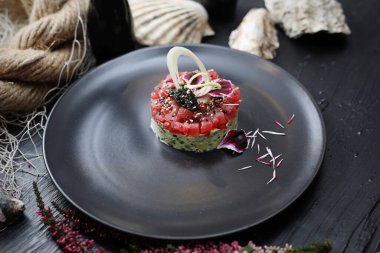 Doğranmış ton balıklı tartar, avokado, havyar ve susam tohumlu, siyah bir tabakta, üst manzara. Balık restoranında nefis bir aperatif..