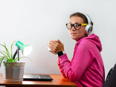 Kulaklık takan, evden çalışan, uzaktan eğitim yapan bir kadın. Kahve içen güzel kız internette video konferansı dinliyor. Masada gözlüklü bir iş kadını.