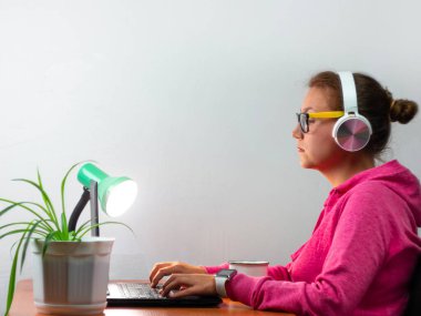 Kulaklık takan, evden çalışan, uzaktan eğitim yapan bir kadın. Kahve içen güzel kız internette video konferansı dinliyor. Masada gözlüklü bir iş kadını.