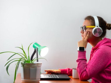 Kulaklık takan, evden çalışan, uzaktan eğitim yapan bir kadın. Yorgun öğrenci kız kahve içiyor internette video konferansı dinliyor. Masada gözlüklü bir iş kadını.