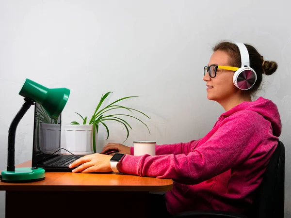 Kulaklık takan, evden çalışan, uzaktan eğitim yapan bir kadın. Kahve içen güzel kız internette video konferansı dinliyor. Masada gözlüklü bir iş kadını.