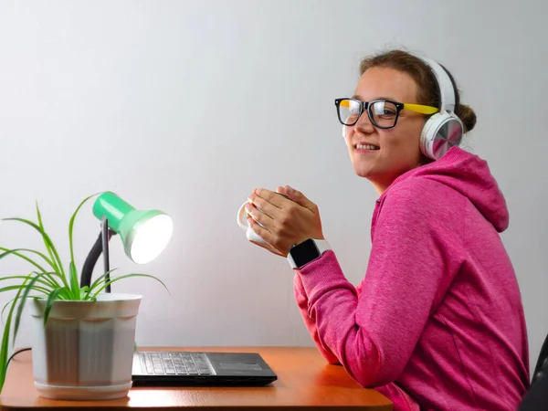 Kulaklık takan, evden çalışan, uzaktan eğitim yapan bir kadın. Kahve içen güzel kız internette video konferansı dinliyor. Masada gözlüklü bir iş kadını.