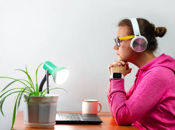 Kulaklık takan, evden çalışan, uzaktan eğitim yapan bir kadın. Yorgun öğrenci kız kahve içiyor internette video konferansı dinliyor. Masada gözlüklü bir iş kadını.