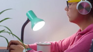 Kulaklık takan, ev uzaklığı öğrenme bürosundan dizüstü bilgisayarda çalışan serbest çalışan bir kadın. Kahve içen güzel kız internette video konferansı dinliyor. Gözlüklü kadın..