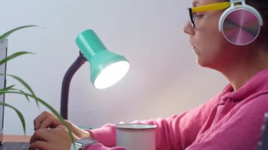 Kulaklık takan, ev uzaklığı öğrenme bürosundan dizüstü bilgisayarda çalışan serbest çalışan bir kadın. Kahve içen güzel kız internette video konferansı dinliyor. Gözlüklü kadın..