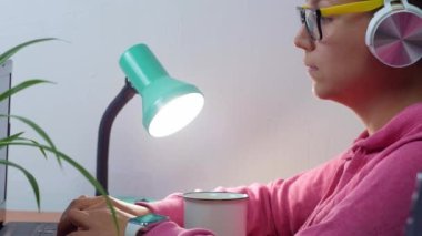 Kulaklık takan, evden çalışan, uzaktan eğitim yapan bir kadın. Gülümseyen öğrenci kız kahve içiyor internette video konferansı dinliyor. Masada gözlüklü bir iş kadını.