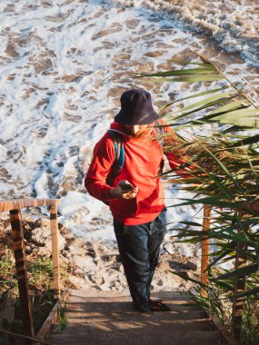 Sakallı milenyum adamı kırmızı kapüşonlu sırt çantasında akıllı telefonuyla sonbahar kuru sazlıklarının fotoğrafını çekiyor. Otantik erkek turist blogcu adam yaşam tarzı Solo seyahat macera konsepti aktif sırt çantası