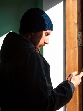 Sakallı, siyah yağmurluk giymiş, elinde akıllı telefonuyla duvara sert gölgeyle mesaj atan bin yıllık bir adam. Otantik erkek gezgin blogcu adam yaşam tarzı Solo seyahat macerası. Günlük iletişimi