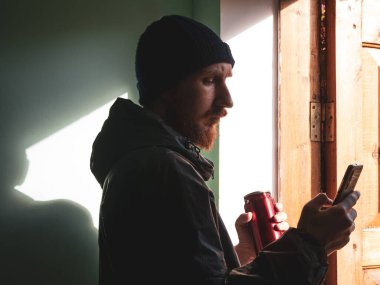 Sakallı, siyah yağmurluk giymiş, elinde akıllı telefonuyla duvara sert gölgeyle mesaj atan bin yıllık bir adam. Otantik erkek gezgin blogcu adam yaşam tarzı Solo seyahat macerası. Günlük iletişimi