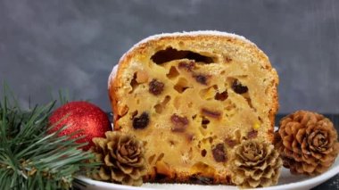 Noel meyveli kekin üzerine koyu arkaplan üzerine pudra şekeri döküldü. Şenlikli pasta pişirme. Çalıntı hamur tarifi malzemeleri fındıklar kurutulmuş şekerli meyve yumurtası kepekli un kurutulmuş meyve yağı. Yeni yıl dekorasyon masası servisi.