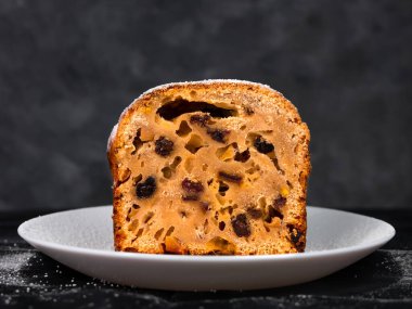 Noel meyveli keki pudra şekeri beyaz tabakta koyu arka planda mevsimlik süslemeler. Xmas atmosferik tebrik kartı. Şenlikli hamur işi pişirme, kek hamuru tarifi, kurutulmuş şekerli meyveler.