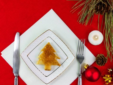 Noel masası beyaz tabak çatal bıçak takımına tost koyuyor kırmızı masa örtüsü arka planda düz duruyor. Yılbaşı partisi restoran dekorasyonu Kış tatili tebrik kartı tasarımı