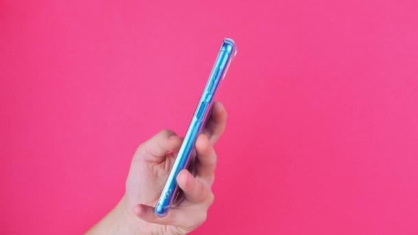 ピンクの色の背景にブロガーの手のスマートフォン スクロールページ タッチスクリーン側のビューをタップします 通信を利用したターコイズ携帯電話 オンラインビジネスソーシャルメディアブログのテキストメッセージ — ストック動画