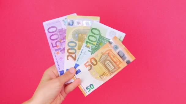 ハンドインはピンク色の背景に50 100 200と500ユーロのお金の請求書を保持しています 現金ヨーロッパの銀行券を数える 節約を稼ぐ ユーロ通貨交換富の概念 オンラインカジノ勝者ビジネス取引 — ストック動画