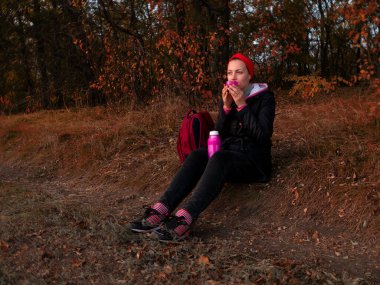Gezgin kız dağ ormanlarında bitki çayı içer. Turist milenyumu kadınları fincandan sıcak kahve içerek manzaranın tadını çıkarırlar. Seyahat yürüyüşü konsepti. Aktif sağlıklı yaşam tarzı