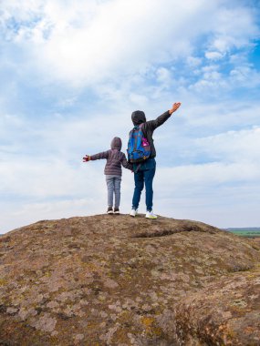 Gezginlerin baba kızı ellerini kaldırarak dağ zirvesine tırmanıyor ve gökyüzünün mavi bulutlu manzarasının keyfini birlikte çıkarıyor. Aktif Yaşam Tarzı Aile Seyahat Manzarası Gezisi Sırt Çantası Yürüyüşü