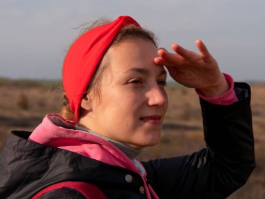 Sırt çantalı gezgin kadın yaban otlarıyla yürüyüş yolunda yürüyor. Kırmızı bantlı kız sırt çantalı, manzaralı mavi gökyüzünün tadını çıkarıyor. Aktif sağlıklı yaşam tarzı turizm Solo Seyahat