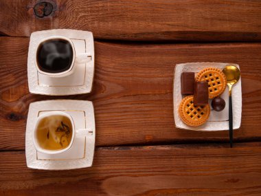 Buğulanmış kahve ve beyaz çay fincanlarıyla ahşap masada şekerleri. Sıcak taze demlenmiş espresso ve bitkisel karışım. Çıtır çerezler çikolatalı şekerler üst tabakta. Restoran içkileri lezzetli kahvaltı menüsü.