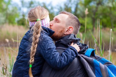 Baba ve kızı göl kenarında oturmuş doğa manzarasıyla sarılıyorlar. Saçları örgülü küçük sarışın kız babasıyla dışarıda yürüyor. Sevgi dolu çocuk, babayı kucakla. Babalar Günü, özgün aile, aşk yürüyüşü.