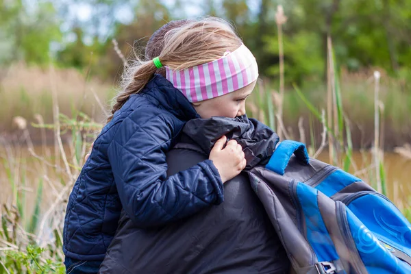 Baba ve kızı göl kenarında oturmuş doğa manzarasıyla sarılıyorlar. Saçları örgülü küçük sarışın kız babasıyla dışarıda yürüyor. Sevgi dolu çocuk, babayı kucakla. Babalar Günü, özgün aile, aşk yürüyüşü.