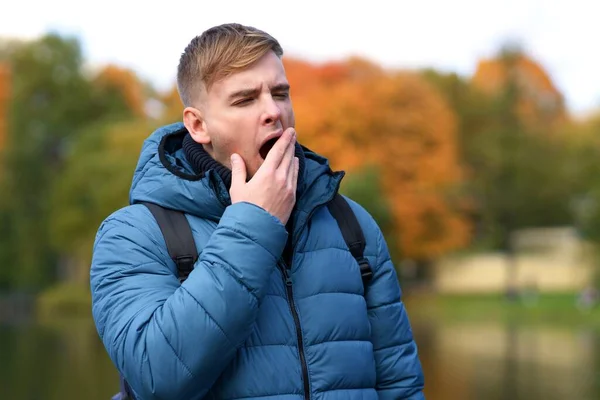 Portrait de fatigué fatigué endormi bel homme, jeune type bâillant est bâiller avec sa bouche ouverte couvrant avec la main, se sentant somnolent. Manque de sommeil. Promenade dans le parc d'automne doré. Somnolence, insomnie — Photo