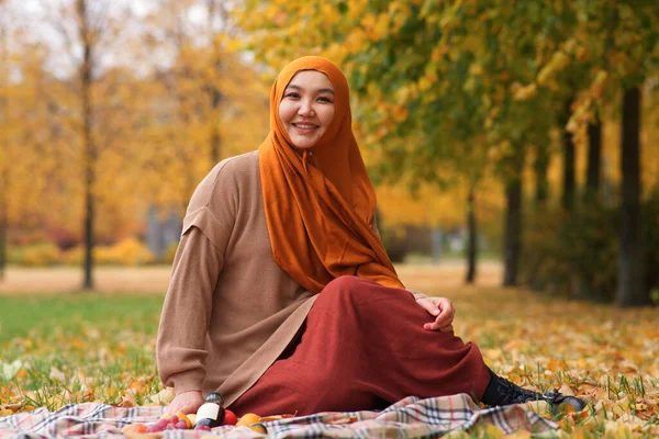 Portrait of beautiful pretty Asian Muslim young woman , Islamic girl is wearing on head hijab scarf sitting on grass, colourful leaves in golden autumn, fall park. Traditional Muslim Arabian clothes — Stock Photo, Image