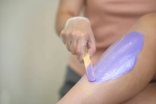 Cosmetologist woman applying wax on young girls leg before the epilation or depilation procedure. Girl is lying on a couch in a beauty salon on procedure shugaring Royalty Free Stock Photos