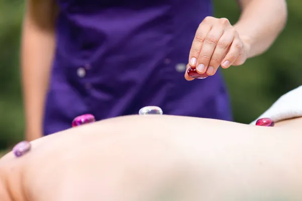 Профессиональная массажистка делает массаж камнями девушке на открытом воздухе в спа-салоне — стоковое фото