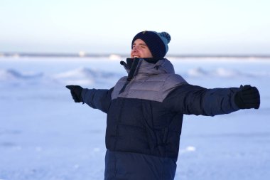 Portrait of handsome happy positive guy young cheerful man is enjoying smiling walking in warm clothes hat coat at winter cold frosty day outdoors open spread his hands wide. Freedom happiness concept